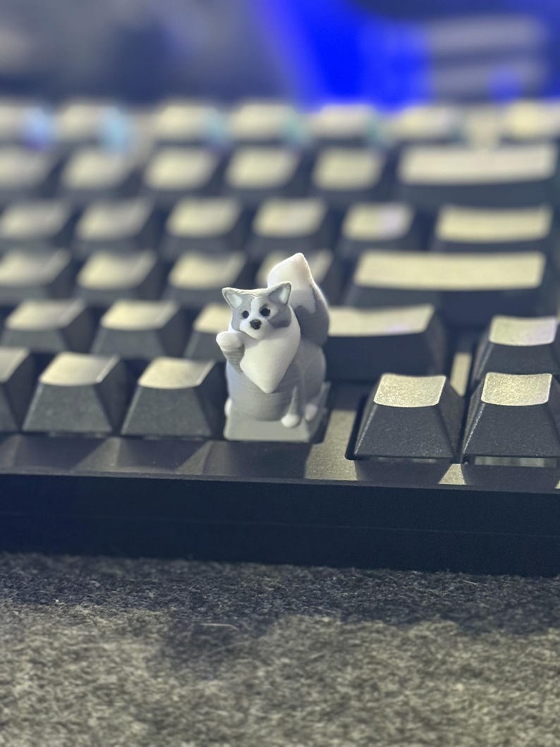 Gray and white cat keycap with one paw raised, installed on a mechanical keyboard