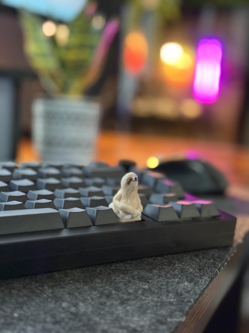 An ivory sloth keycap sitting on a dark mechanical keyboard, with colorful lights behind it